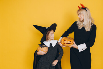 Mother and daughter wearing halloween costumes holding jack o' lanterns posing on yellow background
