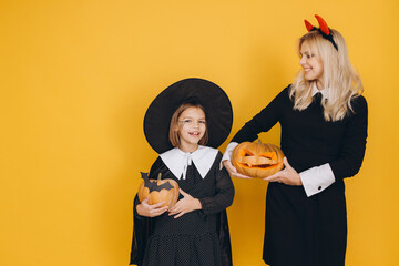 Mother and daughter wearing Halloween costumes holding carved pumpkins