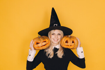 Smiling witch holding two jack o' lanterns celebrating Halloween on yellow background