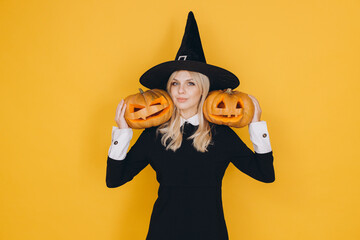 Woman wearing witch costume holding two jack o' lanterns on yellow background