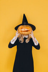Woman wearing witch costume holding carved pumpkin in front of face
