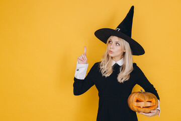 Young witch pointing up and holding a carved pumpkin for Halloween celebration