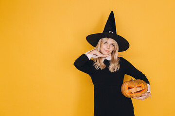 Pensive witch holding carved pumpkin celebrating Halloween on yellow background