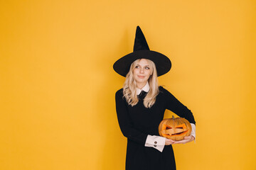 Smiling witch holding jack o' lantern looking up on yellow background