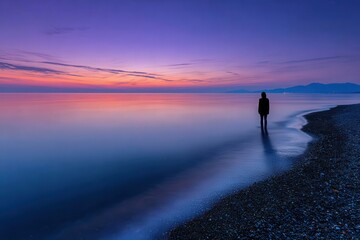 Fototapeta premium Silhouette of person stands on pebble beach at dusk in Turkey