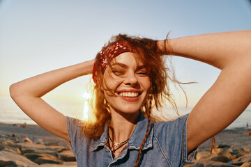 smiling woman enjoying sunset at the beach with carefree expression and red bandana hair accessory,...
