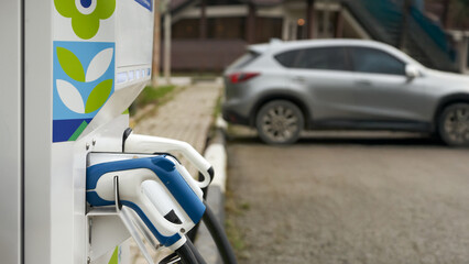 Element of transport infrastructure. Fragment of an electric charging station with charging ports. In the background is a hybrid electric car.