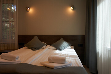 A fragment of a hotel room. A double bed with over-bed lamps. Mountain pines are reflected in the glass of the door.