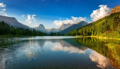Fototapeta premium a serene mountain landscape with golden sunlight lush forests and calm lake reflections under a partly cloudy blue sky