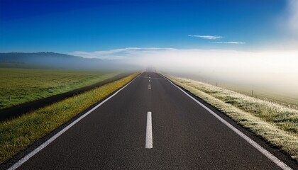 Fototapeta premium foggy haze blankets the landscape as the empty road stretches towards the horizon under a bright blue sky