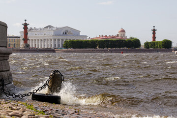 A view of the Neva River with a tire mooring, Rostral Columns, and a historical building on the opposite bank in Saint Petersburg.