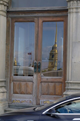 The reflection of the Peter and Paul Fortress spire and flag is visible in the wooden doors of a historic building in Saint Petersburg.
