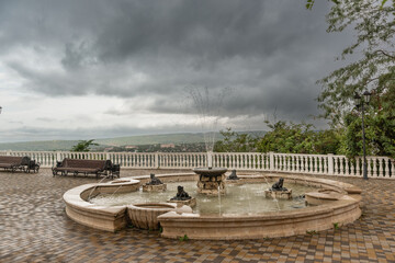 A deserted observation deck with benches and fountain over the resort town of Pyatigorsk on a cloudy autumn day. Rain clouds over the city