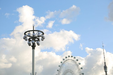 Beautiful summer blue sky with street metal design lamps and ferris wheel on blue clouds background...