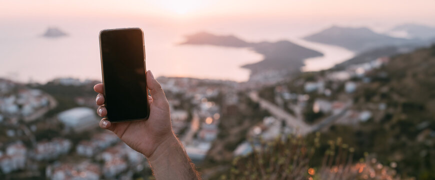 A man shoots a sunset on a mountain by the sea.  Close-up of men's hands with a phone on the background of a sunset landscape