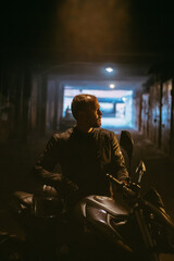Portrait of a man in an outfit with a helmet and a motorcycle in a dark tunnel.
