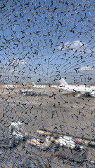 Cracked safety glass with an abstract web-like pattern, shot against a blurred airport scene. A...