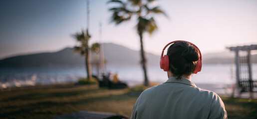 Portrait from the back of a young man in bright big headphones by the sea at sunset. A handsome guy...