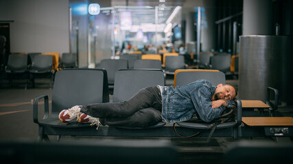A tired male passenger sleeps on the seats waiting for boarding in the departure area of the...