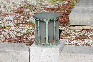 An octagonal, weathered metal lantern with frosted glass panels sits atop a stone step, surrounded...