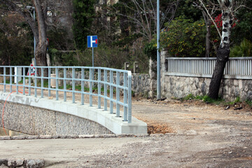 A blue dead end street sign stands at the edge of an unfinished road, bordered by a new metal...