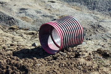 A large, flexible red and black corrugated drainage pipe lies abandoned on cracked, dry soil at a...