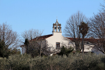 A traditional white church with a red-tiled roof and twin bell tower rises above bare winter trees,...