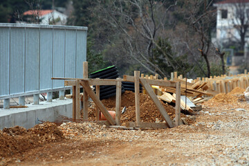 A roadside construction area features wooden formwork, stacked pipes, and scattered earth, with a...