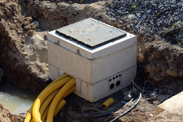 A concrete utility junction box is partially buried at a construction site, with multiple yellow...