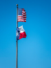 Torn American and Texas flags wave against a clear blue sky.