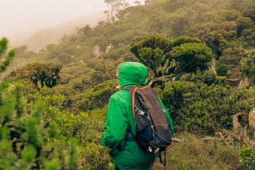 Scenic view of a hiker wearing a waterproof jacket and backpack in the forest on a rainy day in Mount Longido in Tanzania 