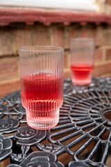 A vibrant pink beverage in ribbed glasses on a designed metal outdoor table, evoking a relaxed summer garden vibe.