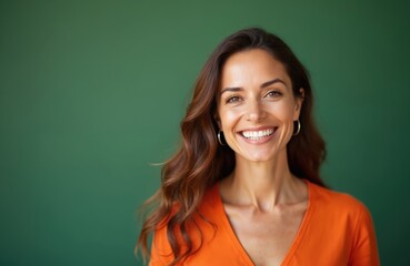 Attractive woman with long brown hair smiles. She wears an orange shirt, showing positive emotions. Cheerful female with radiant happiness expresses pure joy. Portrait photo.