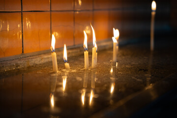 Candles burning in church interior, reflecting on wet surface. Flickering hope in dark. Silent light in still water. Prayer, contemplation and worship concept