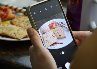 female hands holding smartphone and taking photo of sweet food. photo or video blogger. sweet and tasty dessert for kids and adults. cookies and candies on plate