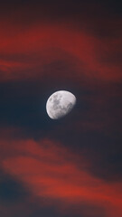 Sharp moon in a red and dark cloudy sky at dusk.