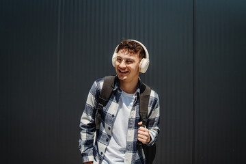 Portrait of a young adult man student smile with wireless headphones on black wall background