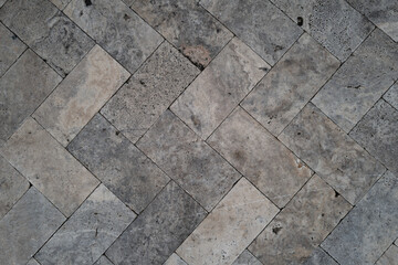 Close-up of a stone tile surface laid in a herringbone pattern, featuring varied textures, pores,...