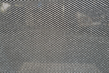 Close-up of a metallic mesh screen forming a repetitive diamond-shaped pattern. The background is softly blurred, emphasizing the texture and geometry of the netting. Ideal for illustrating concepts o