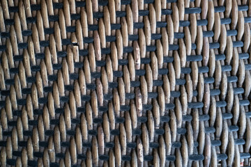 Close-up of a rustic woven texture featuring interlaced natural rattan strands and black synthetic...