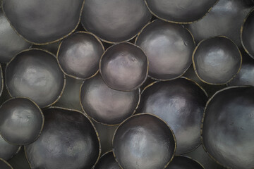 Abstract close-up of clustered metallic black ceramic bowls with subtle sheen and organic contours....