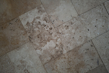 Close-up of a stone tile surface laid in a herringbone pattern, featuring varied textures, pores,...