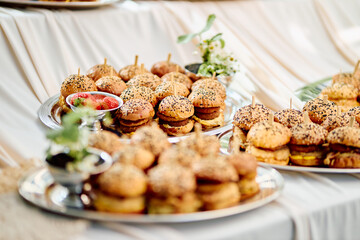 Outdoor mini sandwich platter with sesame seed topping and fresh herbs, arranged on silver trays on...