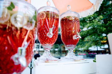 Outdoor strawberry lemonade dispensers with glass lids, filled with vibrant red drink, set in a...
