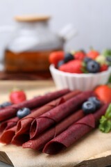Tasty fruit leather rolls, strawberries, blueberries and mint on table, closeup
