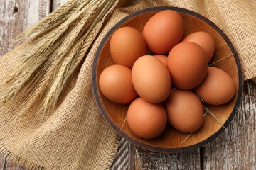 Raw eggs and spikes of wheat on wooden table, flat lay