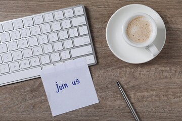 Paper note with words Join Us, cup of coffee and computer keyboard on wooden table, flat lay