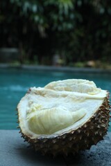 Fresh ripe durian on stone surface near swimming pool outdoors, closeup