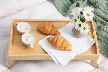 Tray with delicious breakfast and flowers on bed indoors, closeup