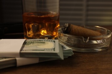 Mafia and criminal world. Money, ashtray with cigar and whiskey on wooden table, closeup
